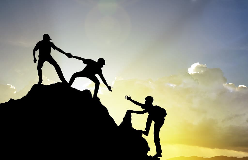 People helping each other climb a mountain